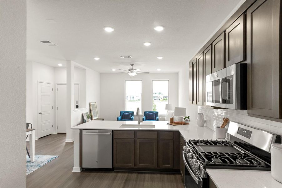 Kitchen with stainless steel appliances, a peninsula, light countertops, dark wood-style flooring, and recessed lighting