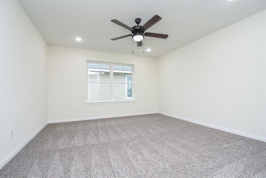 Master bedroom with beige walls, carpeted floor, a window, and a ceiling fan.