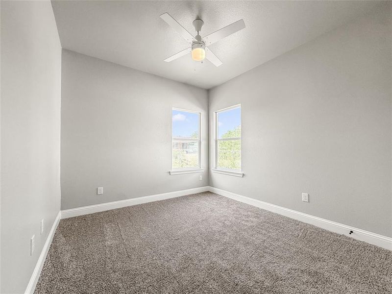 Carpeted room featuring light gray walls, two windows, a white ceiling fan with integrated lighting, and white baseboards Carpeted room featuring light gray walls, two windows, a white ceiling fan with integrated lighting, and white baseboards