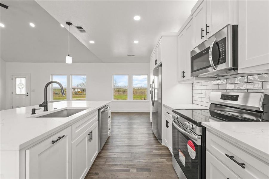 Kitchen with stainless steel appliances, white cabinetry, light stone countertops, and sink