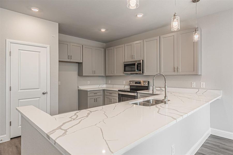 Kitchen with kitchen peninsula, dark hardwood / wood-style floors, appliances with stainless steel finishes, pendant lighting, and sink