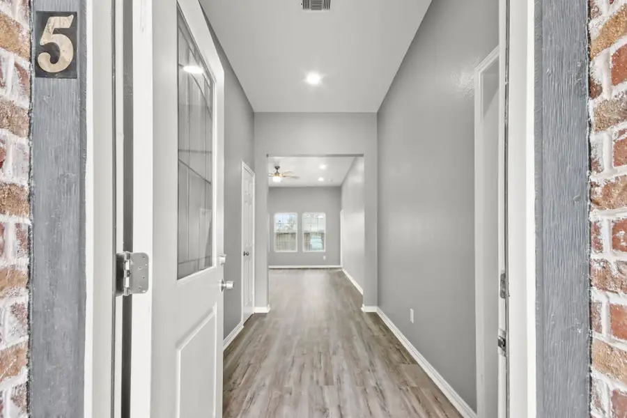 Welcome to your new home! This inviting entryway features sleek hardwood floors, modern gray walls, and recessed lighting. The hallway leads into a bright, open living area with large windows and a ceiling fan, creating a warm and welcoming atmosphere.