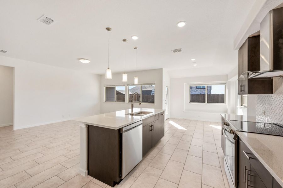 Kitchen with dark cabinets, center island with sink, pendant lights, and tile floors open to living area