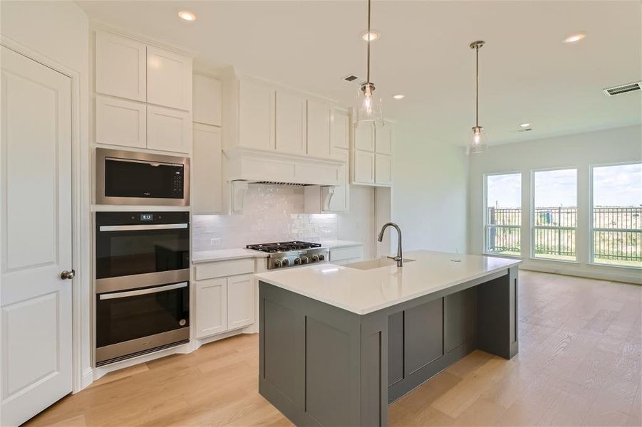 Kitchen featuring light hardwood / wood-style flooring, stainless steel appliances, tasteful backsplash, a kitchen island with sink, and white cabinetry