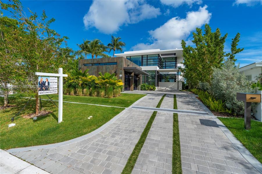 Modern architectural exterior featuring stone-tile cladding, floor-to-ceiling glass windows, and a paved driveway with grass strip accents