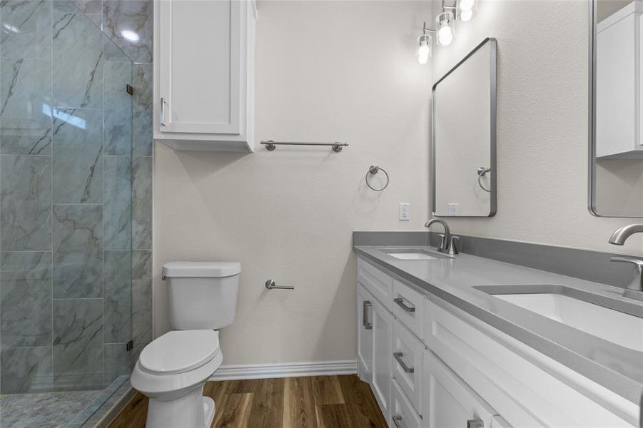 Full bathroom with double vanity, dark wood-style flooring, and a tile shower