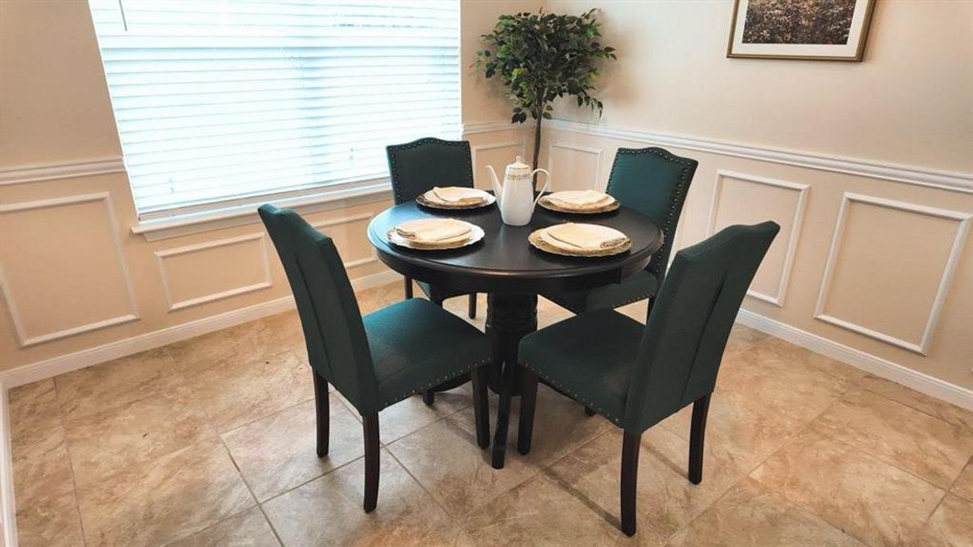 Dining area featuring neutral-toned walls with wainscoting, ceramic tile flooring, and a large window with horizontal blinds
