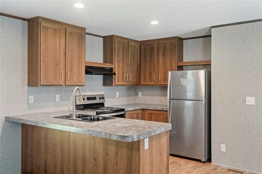 Kitchen with stainless steel appliances, light countertops, a peninsula, light wood-style flooring, and wood finish cabinetry