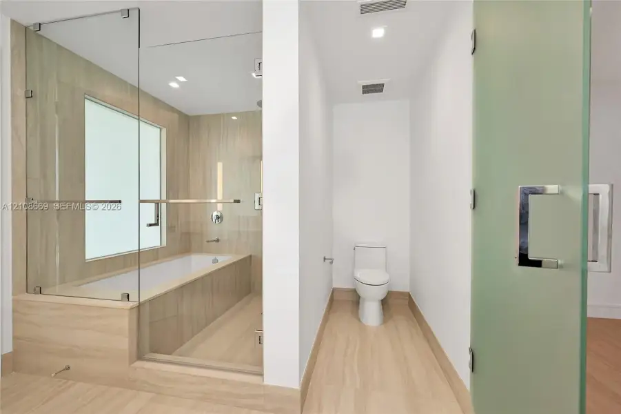 Glass-enclosed soaking tub, tile surround, recessed lighting, and frosted glass door