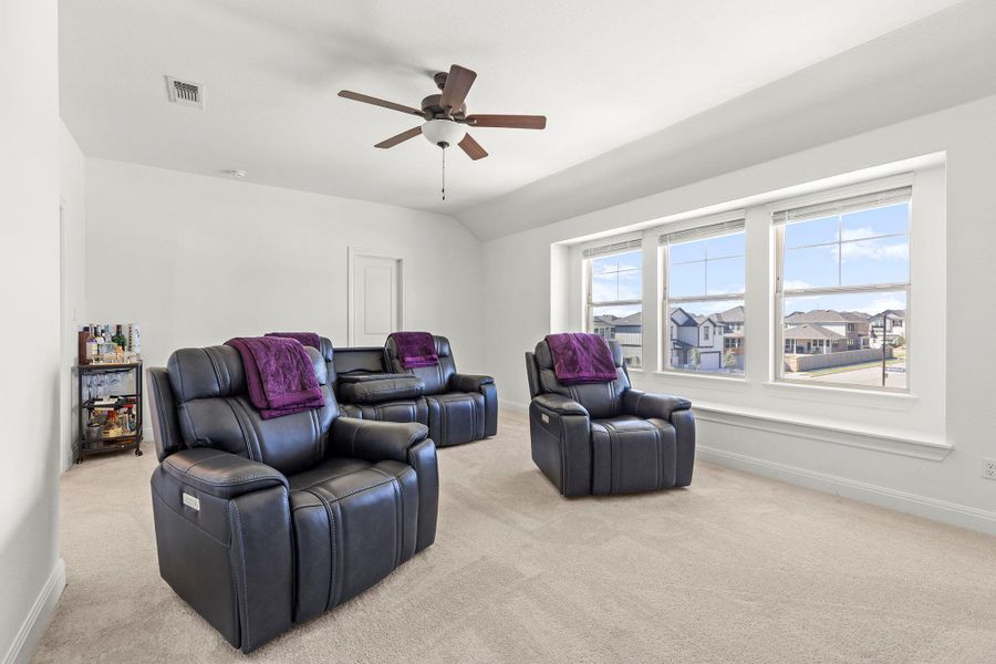 Cinema room featuring light carpet, a ceiling fan, and vaulted ceiling