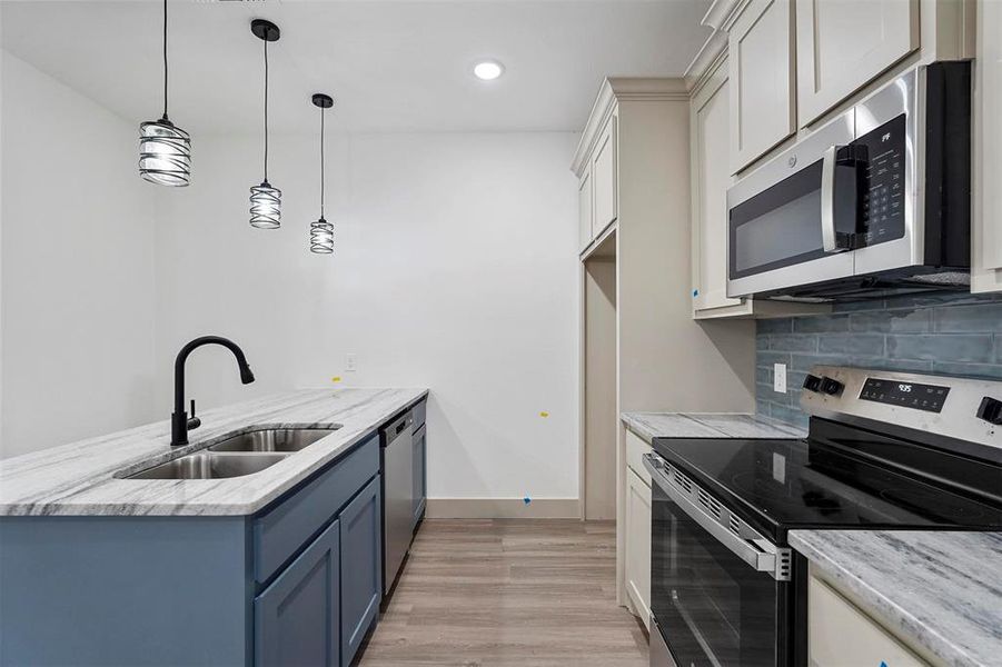 Kitchen with tasteful backsplash, appliances with stainless steel finishes, a peninsula, blue cabinets, and a sink