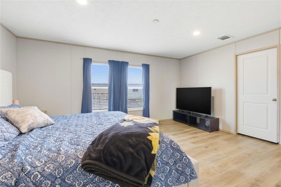 Comfortable bedroom with warm wood-look flooring and bright natural light through wide windows.