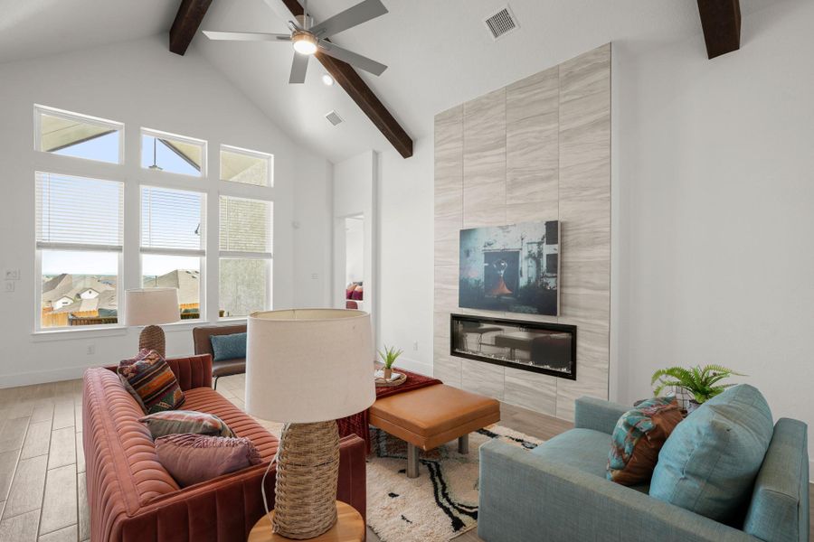 A well-lit living area features high ceilings, exposed beams, and a sleek fireplace with a tile surround.