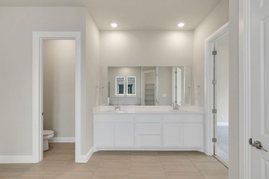 Full bath featuring toilet, double vanity, a sink, and baseboards Full bath featuring toilet, double vanity, a sink, and baseboards