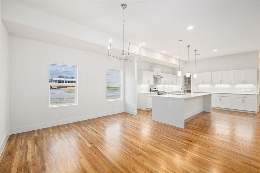 Kitchen with stainless steel gas range oven, light wood finished floors, a center island with sink, a sink, and light countertops