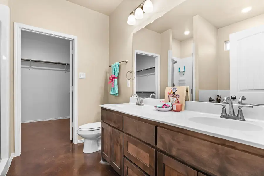 Full bathroom with a walk in closet, a shower stall, concrete flooring, and double vanity
