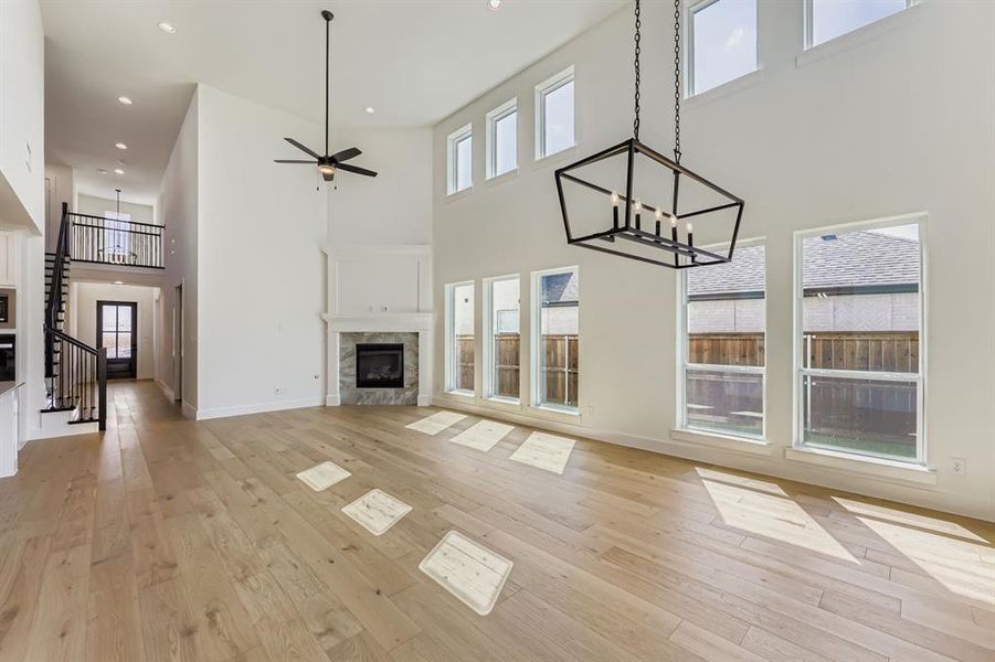 Unfurnished living room with a chandelier, a premium fireplace, a towering ceiling, light wood-type flooring, and a ceiling fan