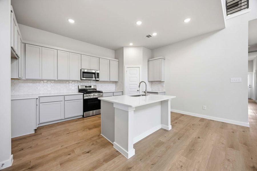 Open kitchen featuring gray cabinets, white island with sink, gas range, and hexagon tile backsplash