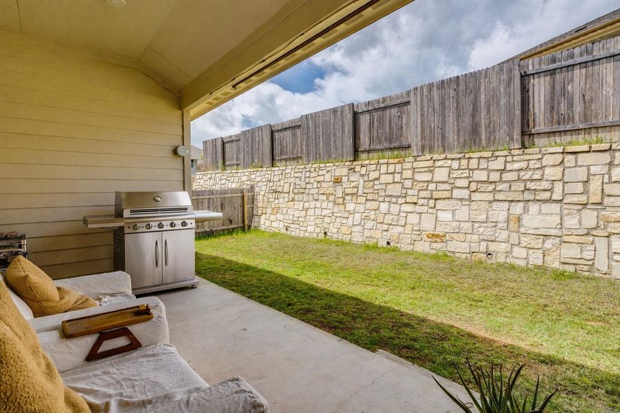 An inviting covered patio opens to a verdant yard, featuring a natural stone retaining wall and privacy fence.