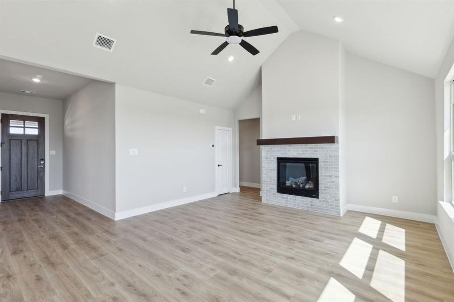 Unfurnished living room featuring visible vents, a brick fireplace, baseboards, light wood-type flooring, and high vaulted ceiling