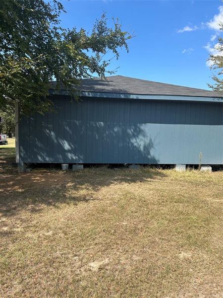 View of side of home with a lawn and roof with shingles