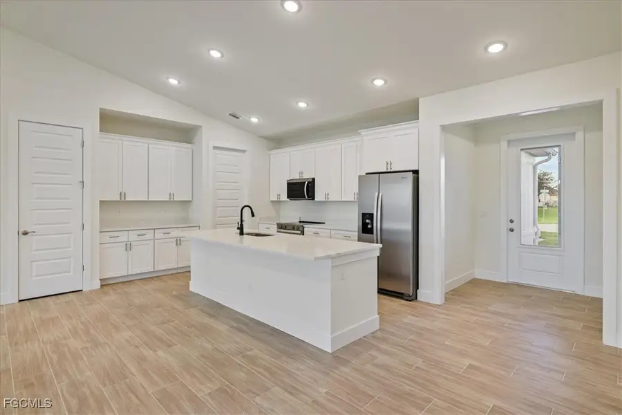 Kitchen with lofted ceiling, stainless steel appliances, white cabinets, a center island with sink, and wood finish floors