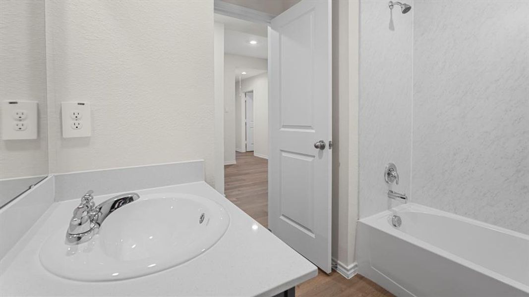 Bathroom featuring a vanity with an integrated sink and chrome faucet, a white bathtub with a shower, and light wood-finish flooring