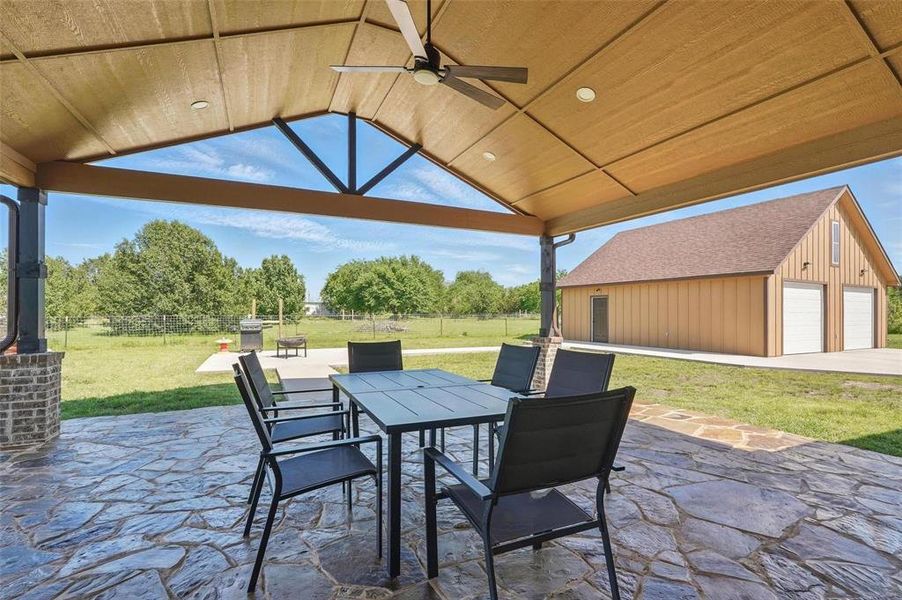 Fenced backyard with a ceiling fan, a patio, outdoor dining area, and an outbuilding Fenced backyard with a ceiling fan, a patio, outdoor dining area, and an outbuilding