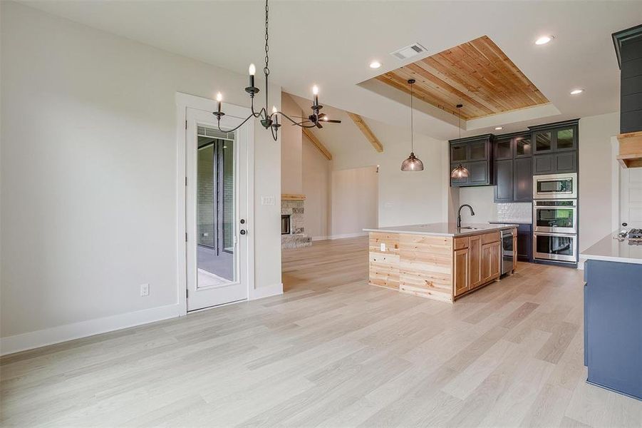 Kitchen with decorative light fixtures, a fireplace, stainless steel appliances, an island with sink, and light wood-type flooring