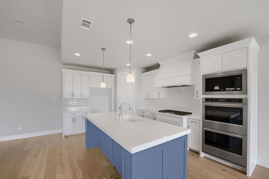Kitchen featuring a central island with a solid surface countertop, white shaker cabinetry, stainless steel appliances, and wood-finish flooring