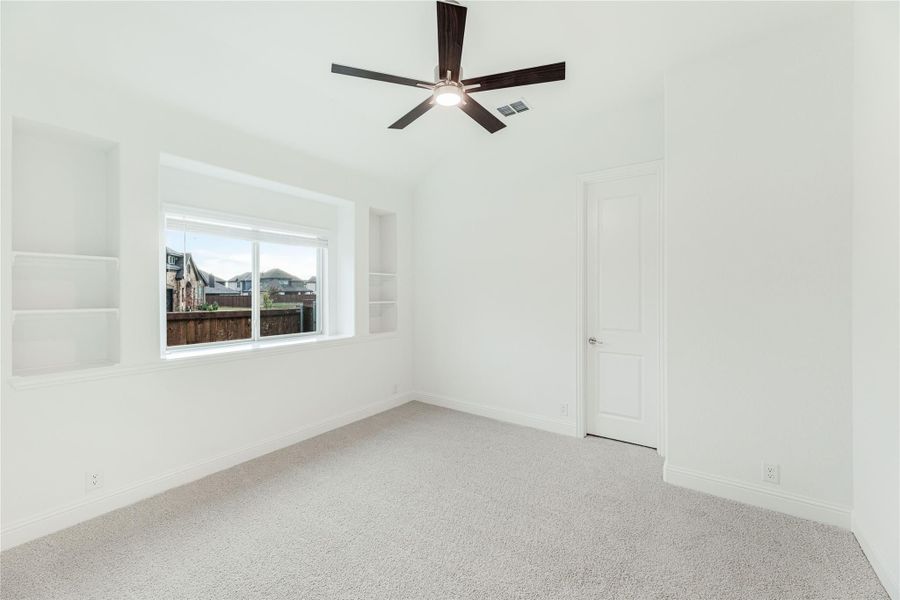 Empty bedroom with carpet, ceiling fan, built-in shelves, and a window with neighborhood view
