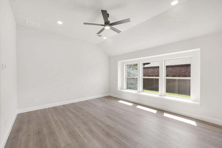 Empty bedroom with vaulted ceiling, ceiling fan, hardwood floors, and large triple window Empty bedroom with vaulted ceiling, ceiling fan, hardwood floors, and large triple window
