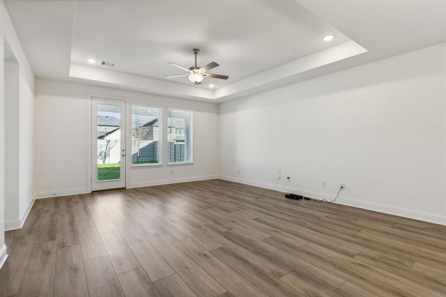 Empty room with ceiling fan, light wood-type flooring, and a tray ceiling