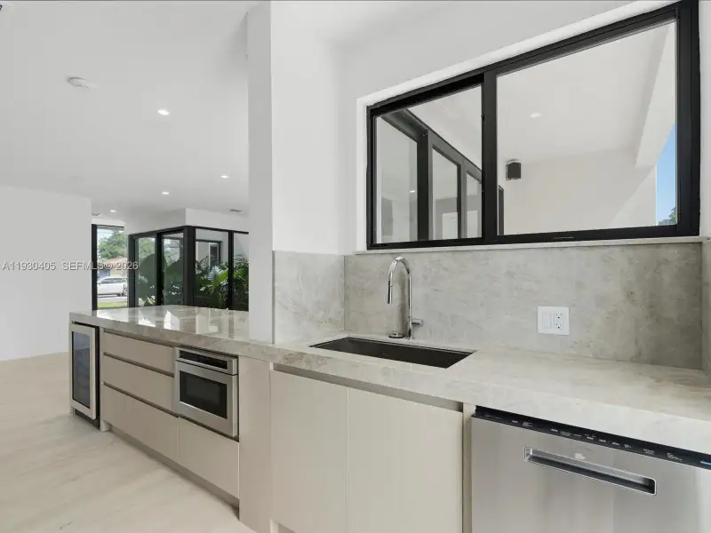 Kitchen featuring stone countertops, integrated stainless steel appliances, a built-in wine refrigerator, flat-panel cabinetry, and black-framed windows Kitchen featuring stone countertops, integrated stainless steel appliances, a built-in wine refrigerator, flat-panel cabinetry, and black-framed windows
