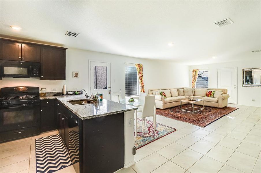 Kitchen with black appliances, light stone countertops, light tile patterned floors, a peninsula, and recessed lighting