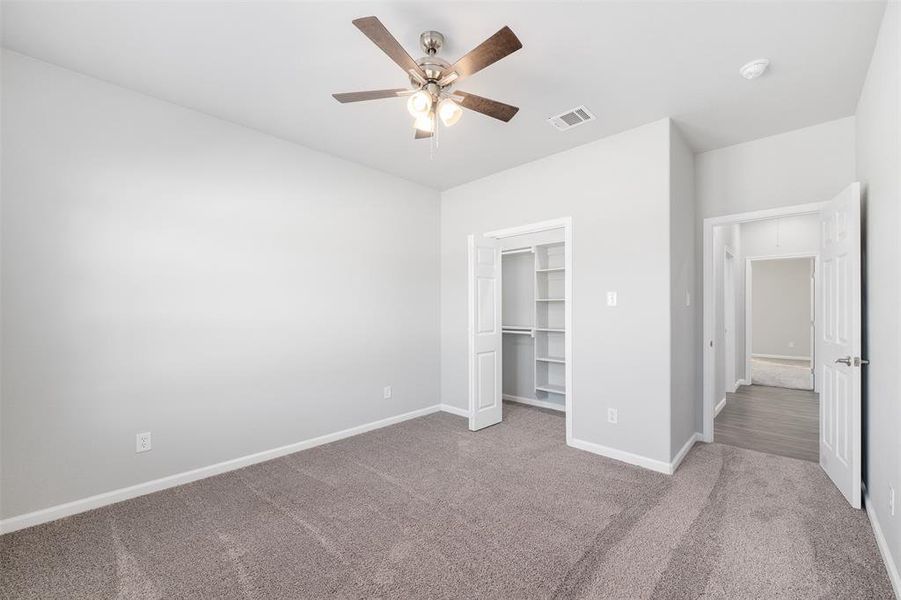 Unfurnished bedroom featuring a walk in closet, carpet flooring, a closet, and ceiling fan