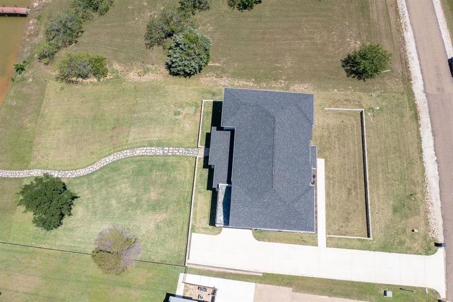 New construction residence featuring a dark shingle roof, a concrete driveway, and a stone-lined pathway