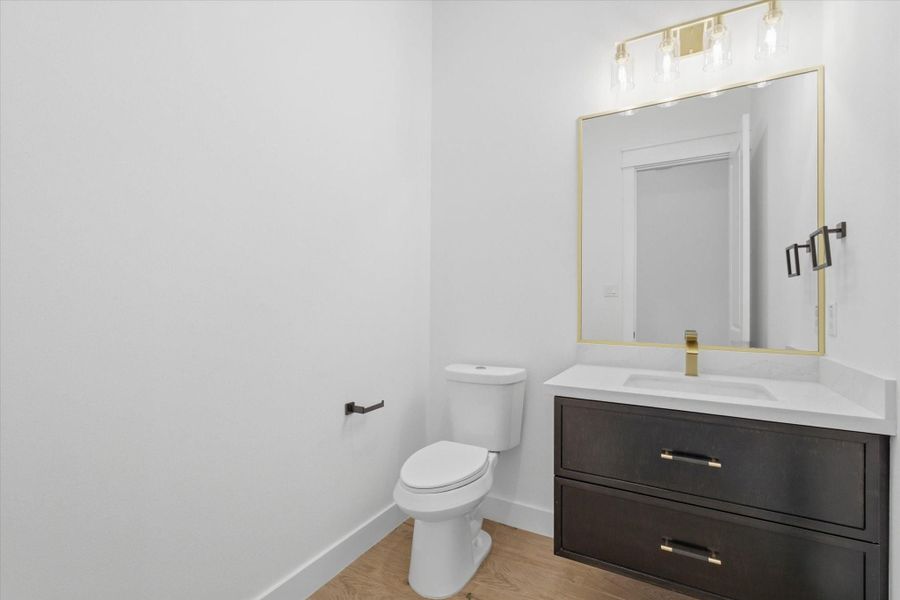 Sophisticated Styling. This chic powder room is sure to impress guests, boasting a deep espresso-finished vanity with modern gold bar pulls, a matching gold-trimmed mirror, and a stunning contemporary multi-light gold vanity fixture.