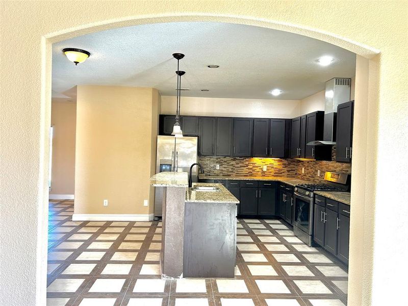 Kitchen with pendant lighting, backsplash, a kitchen island with sink, light stone counters, and stainless steel appliances