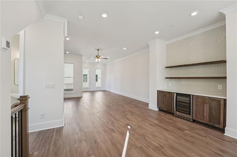 Unfurnished living room featuring ornamental molding, wine cooler, light wood-type flooring, recessed lighting, and ceiling fan Unfurnished living room featuring ornamental molding, wine cooler, light wood-type flooring, recessed lighting, and ceiling fan