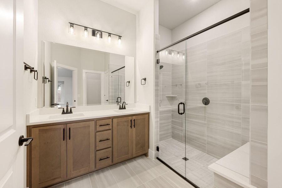 Bathroom with double vanity, wood cabinets, and glass-enclosed tile shower with bench seat Bathroom with double vanity, wood cabinets, and glass-enclosed tile shower with bench seat