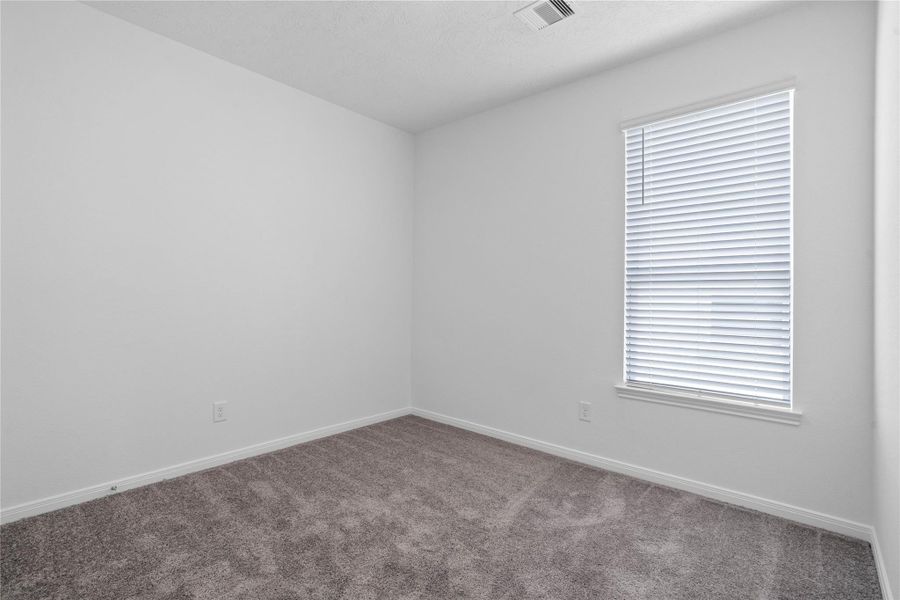Light-filled secondary bedroom complete with cozy carpet flooring, ample closet space, and a large window fitted with blinds.