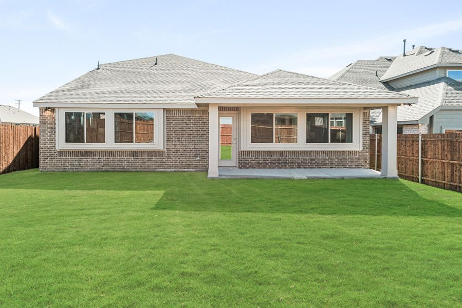 Rear view of single-story brick home with covered patio, large windows, and fenced backyard lawn Rear view of single-story brick home with covered patio, large windows, and fenced backyard lawn