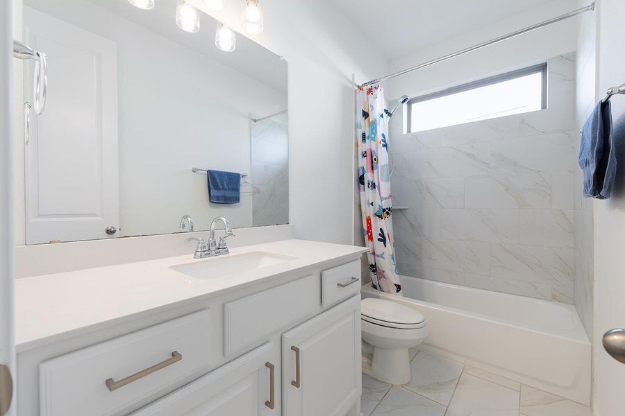 Bathroom featuring shower / bath combo with shower curtain, vanity, and light marble finish flooring