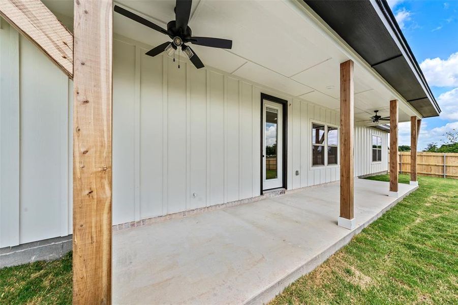 Expansive concrete patio with wood-finish support columns, board-and-batten siding, black ceiling fans, and a glass-paneled exterior door Expansive concrete patio with wood-finish support columns, board-and-batten siding, black ceiling fans, and a glass-paneled exterior door