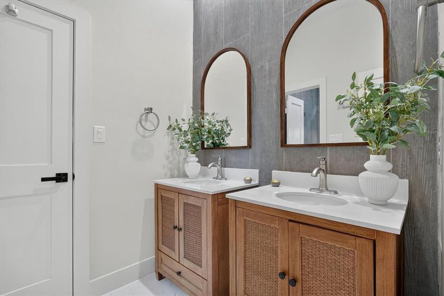 Dual vanity featuring white countertops, undermount sinks, and wood-finish cabinetry with woven cane accents