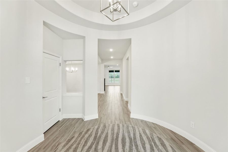 Bright entryway with round tray ceiling, modern chandelier, and light wood floors leading to hallway