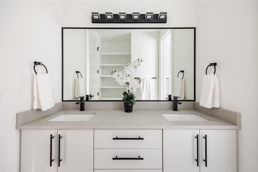 The bathroom features modern lighting and sleek shelving, with black fixtures providing a bold contrast against light cabinets and counters, creating a striking and balanced design.