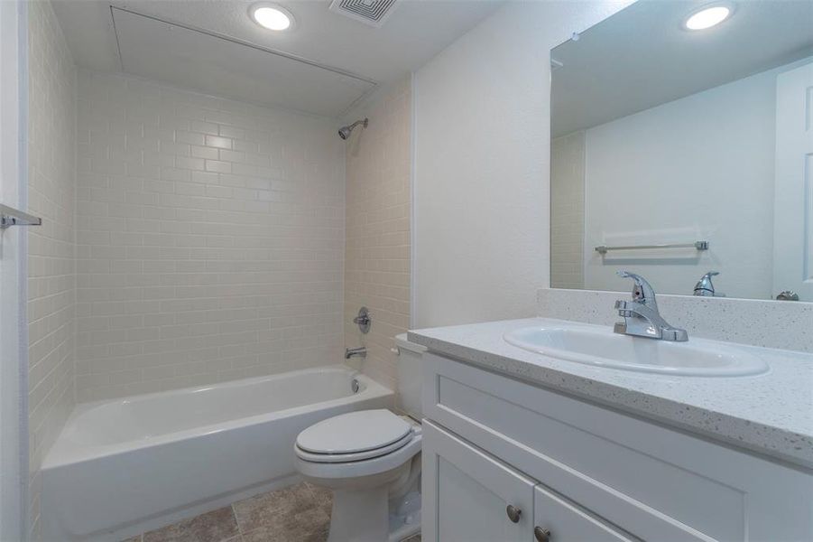 Hall bathroom featuring tiled shower / bath, vanity, toilet, and tile patterned flooring