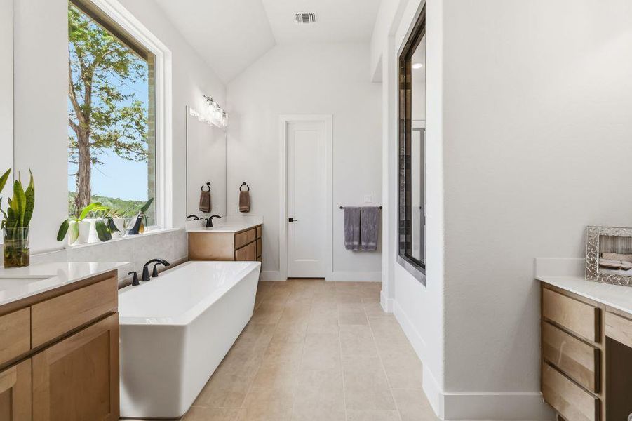 A spacious primary bathroom boasts a freestanding tub, dual vanities, and a large window overlooking natural scenery.